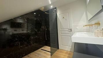 Un baño moderno con pared de mármol negro, puerta blanca y lavamanos de color blanco con detalles dorados.
