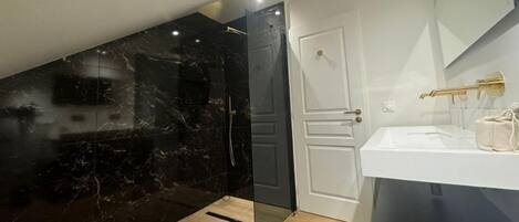 A modern bathroom with a black marble wall, a white door, and a white sink with gold fixtures.