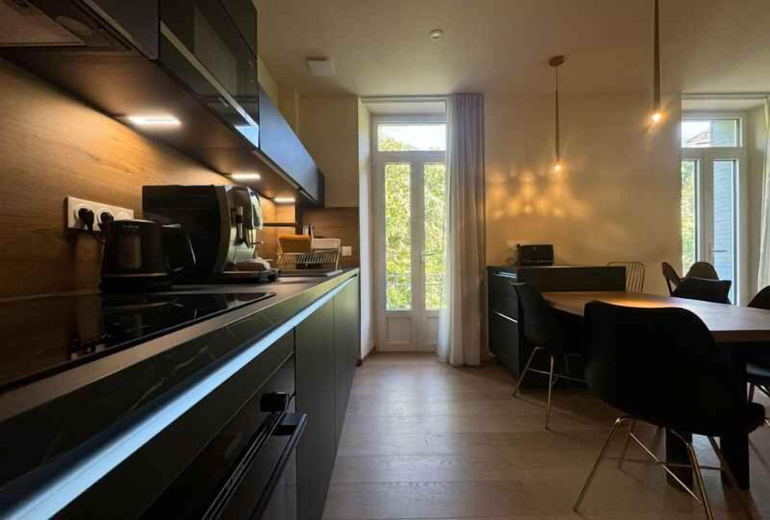 Een moderne keuken met een donker aanrecht, een koffieapparaat en een eethoek met een tafel en stoelen.
