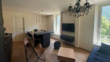 Een moderne woonkamer met een eethoek, een aan de muur bevestigde televisie en een groot raam dat voor natuurlijk licht zorgt.