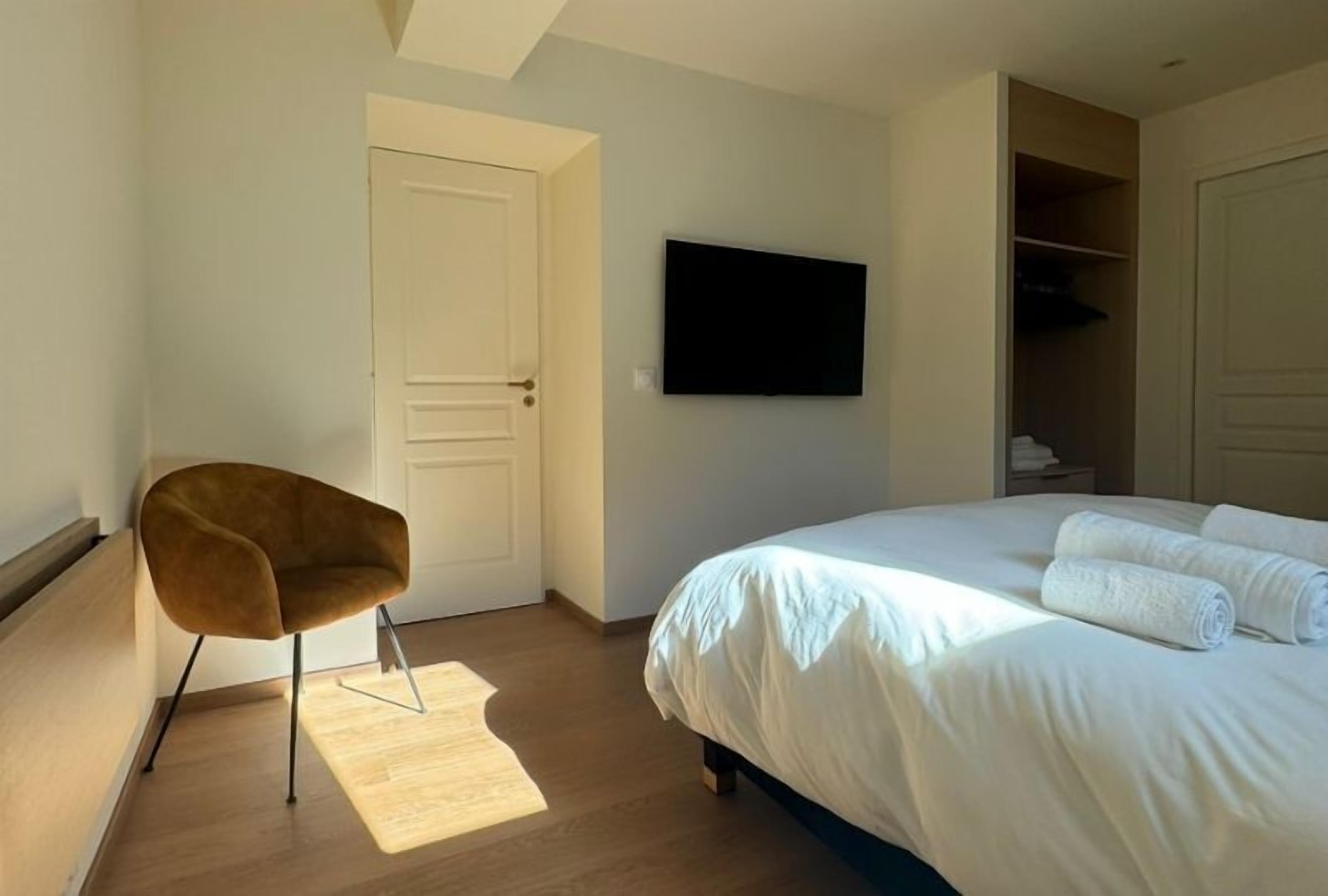 Un dormitorio con cama, una silla, televisor y armario.