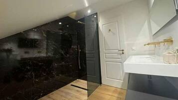 A modern bathroom with a marble wall, a white door, and a sink with a gold faucet.