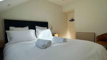 A neatly made bed with white linens and rolled towels, a dark headboard, and a wooden nightstand with a lamp.