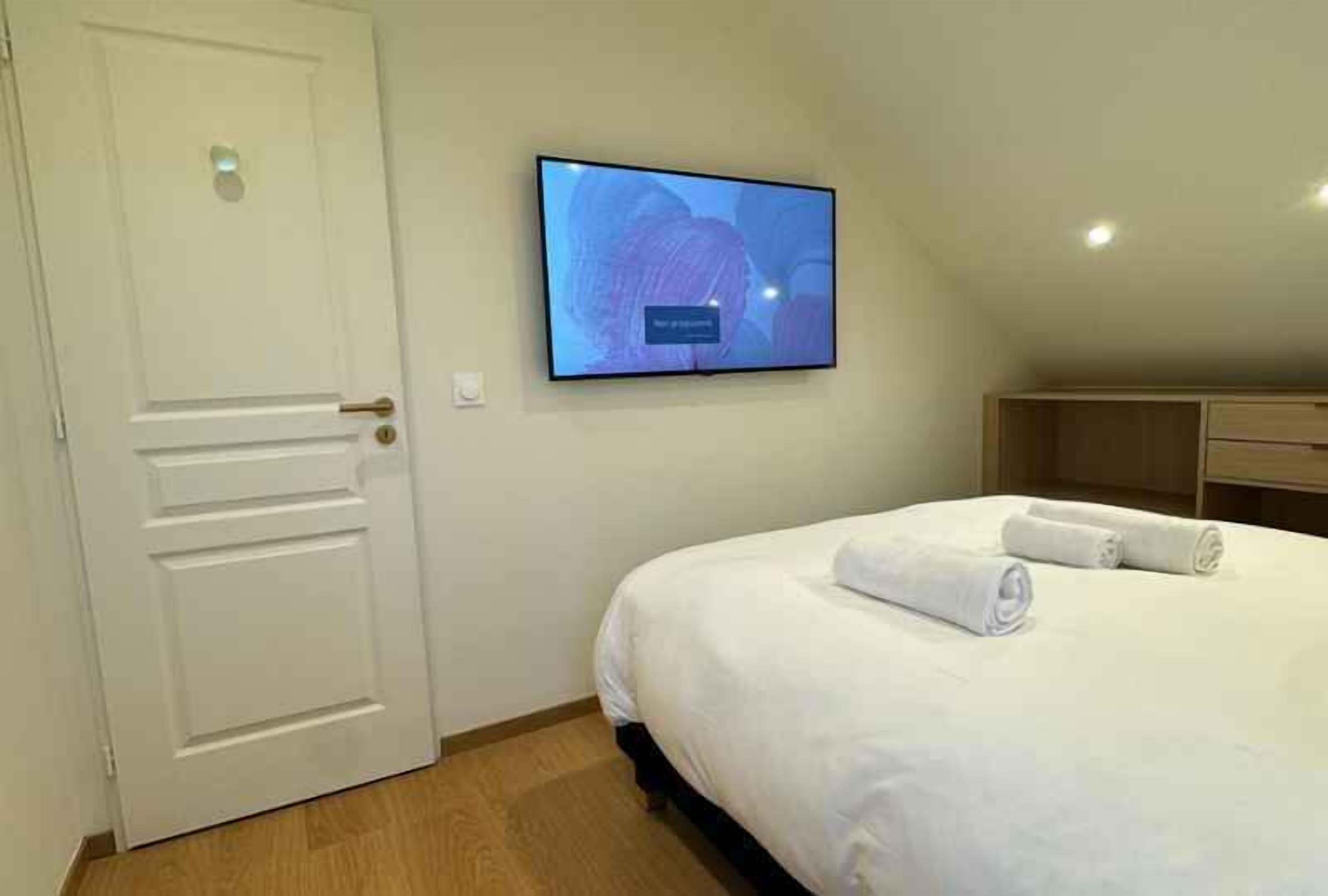 A hotel room with a bed, a flat-screen TV mounted on the wall, and a white door.