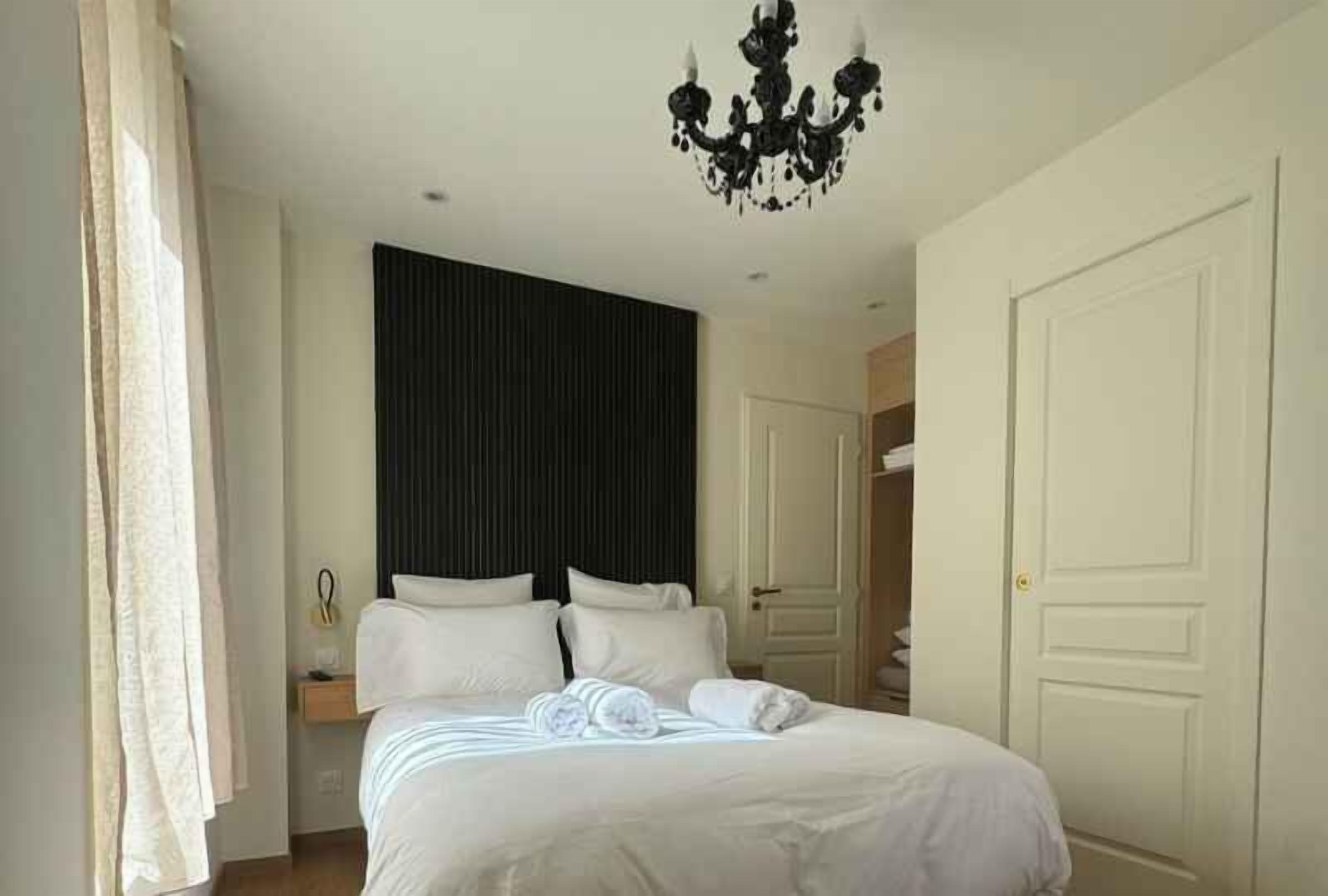A hotel room with a bed, a chandelier, a wardrobe, and a door.