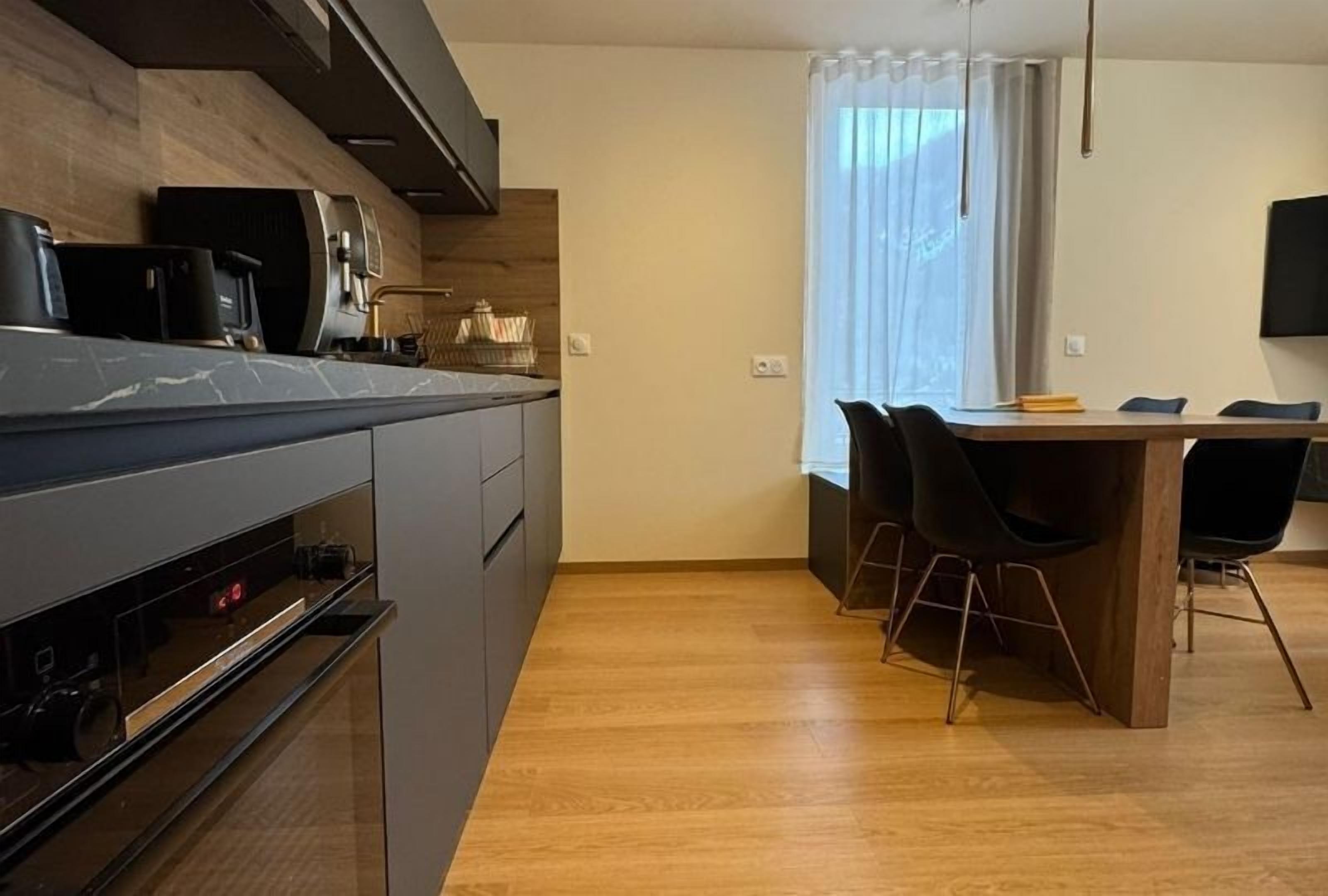 Una cocina moderna con horno integrado y comedor con mesa de madera y sillas negras.