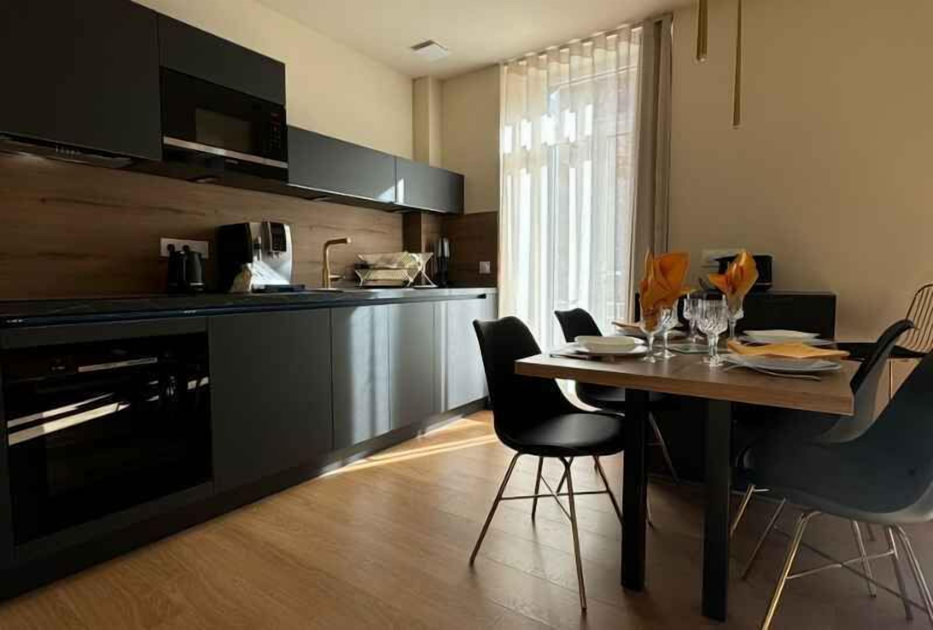A modern kitchen with dark cabinetry, a wooden countertop, and a dining area with a table set for two.