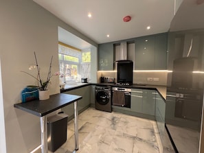 A modern kitchen with a built-in oven, microwave, and dishwasher. There is a window providing natural light, and the floor is tiled. - Family/small Group-wifi-parking-garden-sleeps 6 (Wolverhampton)