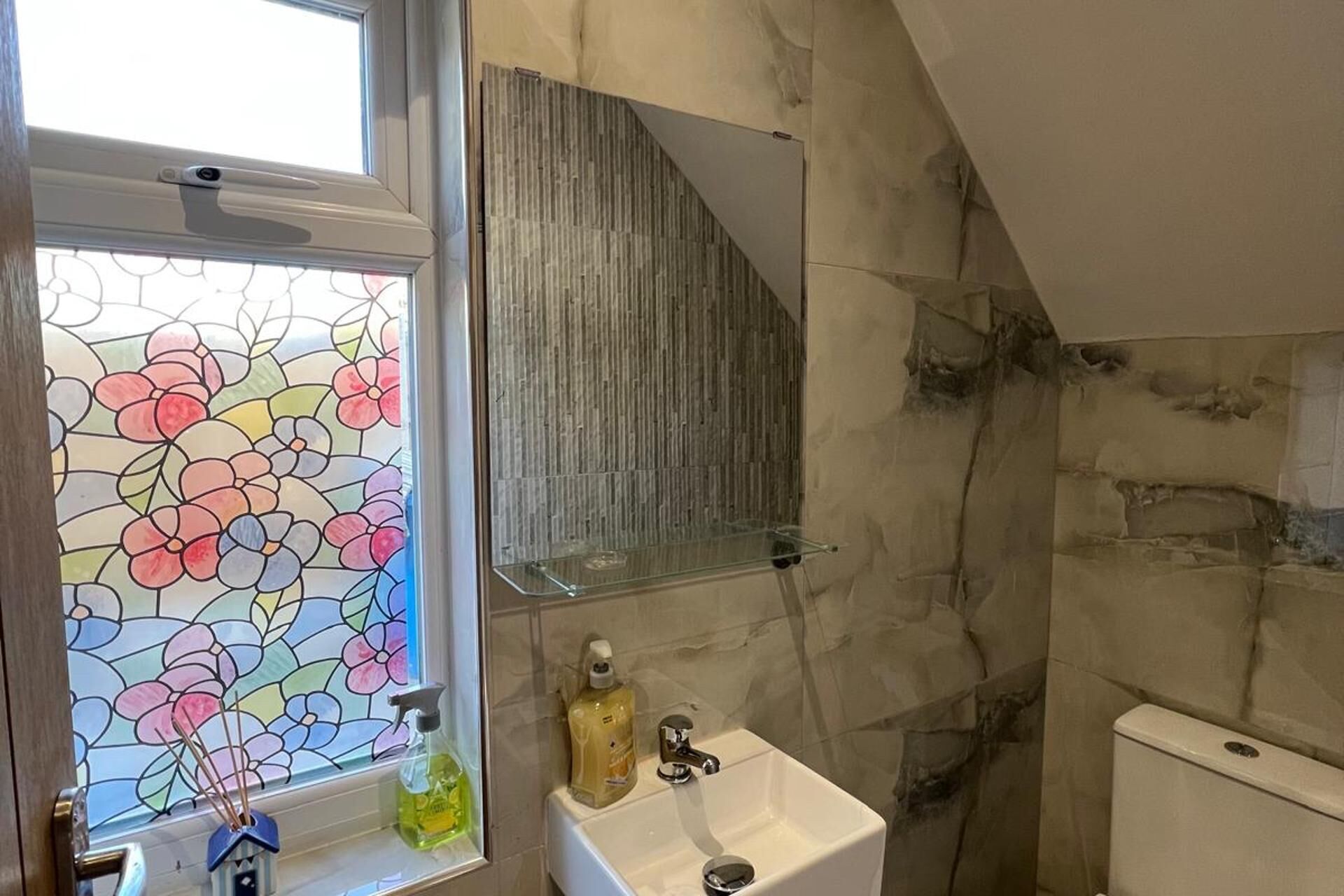 A bathroom with a white sink, a glass shower enclosure, and a stained glass window.
