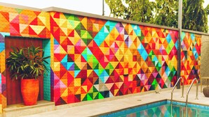 Una piscina con una pared de estampado geométrico colorido y una planta en maceta.