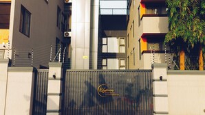 Un edificio moderno con entrada protegida por un portón, un logo visible y una cerca metálica.