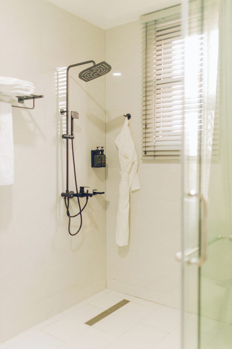 A glass-enclosed shower with a handheld showerhead, a towel rack, and a small shelf with toiletries.