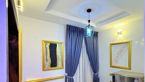 A room with a marble floor, two chairs, a small table, a refrigerator, and two framed artworks on the walls.