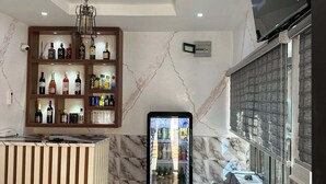 A hotel lobby with a marble floor, a bar area with shelves of liquor, a refrigerator, and a mounted TV.