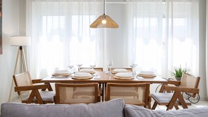A dining area with a round table set for four, surrounded by wicker chairs, a hanging light fixture, and sheer curtains. - Veliero Blu | Kos Marina (Kos)