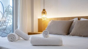 A neatly made bed with rolled white towels, a wooden headboard, and a hanging light fixture. - Veliero Blu | Kos Marina (Kos)