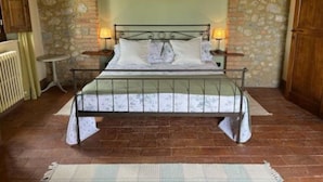 Quarto com arco de pedra sobre a cama, estrutura de cama em metal, duas mesas de cabeceira com luminárias e guarda-roupa de madeira.