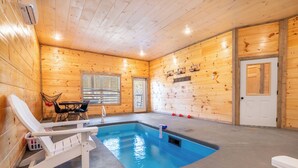 Una cabaña de madera con piscina, una silla de descanso y una mesa con sillas.