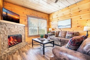 Ein gemütliches Wohnzimmer mit Kamin aus Stein, Holzwänden, einer bequemen Couch und einem Fernseher.