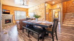 Interior de una cabaña de madera con una mesa de comedor, bancos, chimenea, sofá y una escalera.