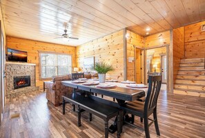 Ein Holzblock-Innenraum mit Esstisch, Bänken, Kamin, Sofa und Treppe.
