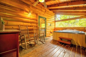 Ein Interieur einer Holzhütte mit Whirlpool, Schaukelstühlen und einem Fenster mit Blick auf Bäume.