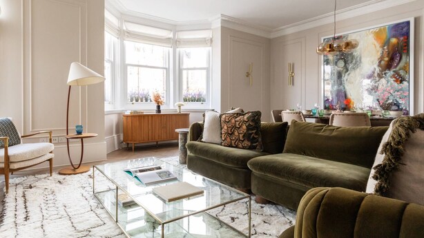 Ein geräumiges Wohnzimmer mit großem Fenster, einem Glastisch und einem grünen Sofa.