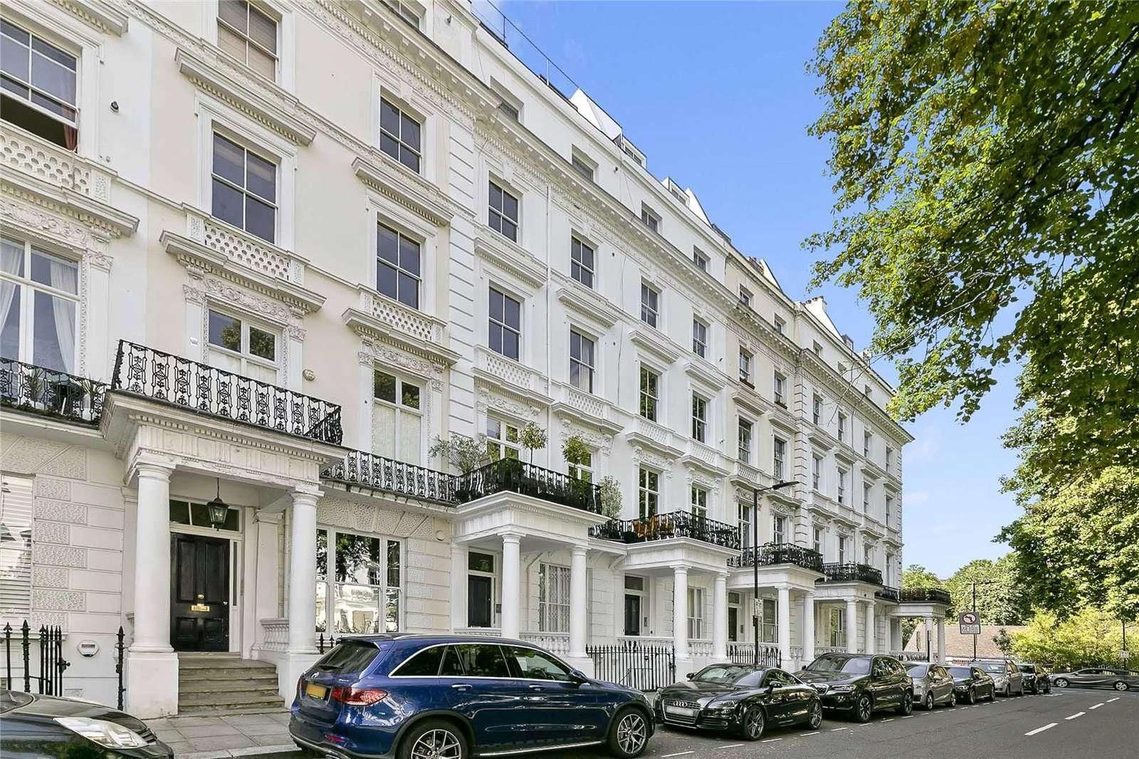 A row of white townhouses with balconies, parked cars, and a clear sky.