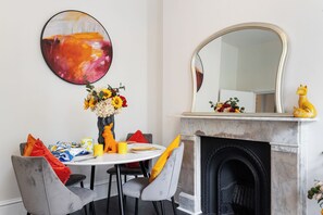 Ein Essbereich mit einem runden Tisch, grau gepolsterten Stühlen, einer Blumenvase und einem Kamin mit Spiegel darüber.