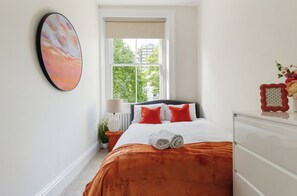 Ein Schlafzimmer mit Bett, Fenster, Heizkörper, Nachttisch und Wandbild.
