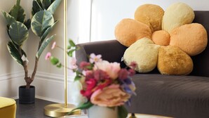 Un salon moderne avec une table basse ronde en verre, un lampadaire, une plante en pot et un canapé doté d’un coussin au design original.