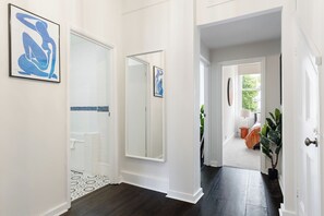 Ein Flur mit dunklem Holzboden, weißen Wänden und einer Tür zu einem Badezimmer mit einer weißen Badewanne und einer gefliesten Duschkabine.