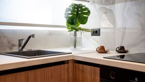 Une cuisine moderne avec un évier à deux bacs, des meubles en bois, une grande plante verte dans un vase en verre et deux tasses à café posées sur le comptoir.