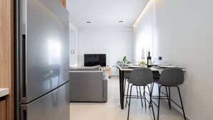 Une cuisine moderne dotée d’un réfrigérateur encastré, un coin repas avec une table et des chaises, et un canapé à l’arrière-plan.