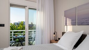 Une chambre d’hôtel comprenant un lit, une table de chevet, une table avec des chaises, et donnant sur un paysage verdoyant et des bâtiments, le tout visible à travers une porte-fenêtre coulissante.