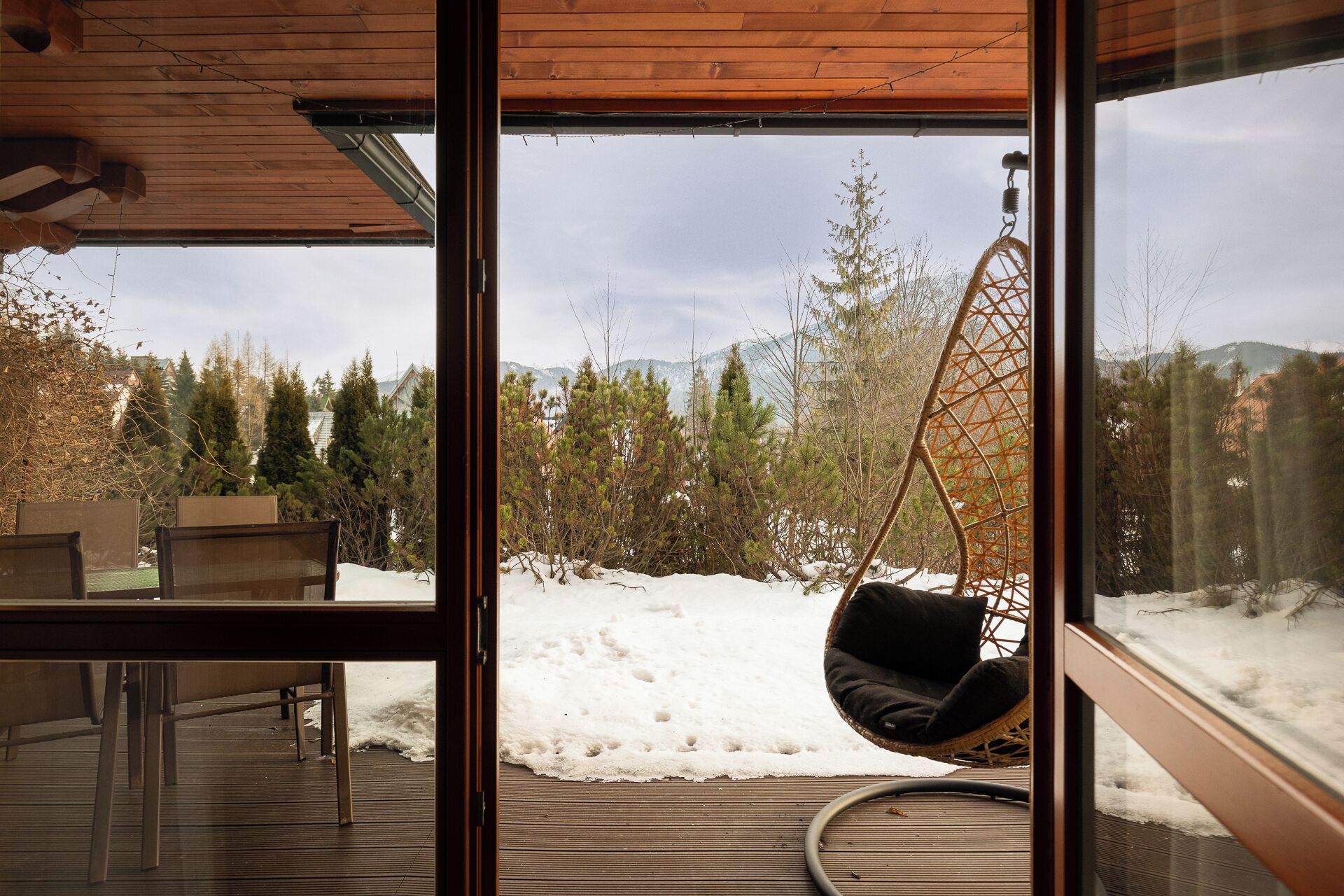 Una habitación con un ventanal grande, una silla colgante y vistas a un paisaje nevado con árboles y montañas.
