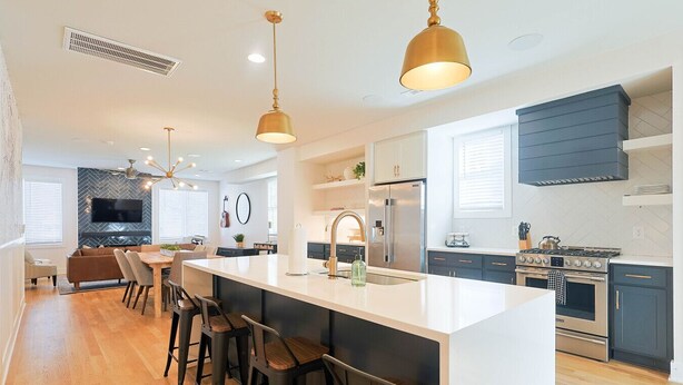 A modern kitchen with a central island, bar stools, stainless steel appliances, and pendant lighting. - Luxury East Nashville Townhome | Walk to Five Points | Dual King Suites & Arcade Room (Nashville)