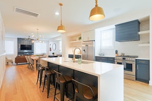 Een moderne keuken met een centraal kookeiland, barkrukken, roestvrijstalen apparatuur en hanglampen.