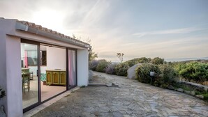 Une maison moderne dotée d’une terrasse en pierre, d’une porte vitr ée donnant sur une pièce comprenant une cuisine, et offrant une vue sur la campagne.