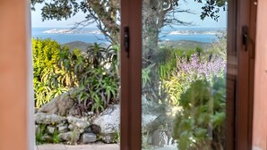 Une vue à travers une porte vitrée, avec un mur de pierre, de la verdure et une côte lointaine.