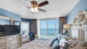 A bedroom with a large bed, a ceiling fan, a television, a chair, and a view of the ocean. - Last minute booking discounts! 2 Bedroom, Beachfront Condo & Free Beach Chairs (Panama City Beach)