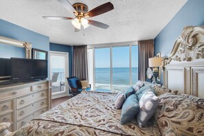 A bedroom with a large bed, a ceiling fan, a television, a chair, and a view of the ocean. - Last minute booking discounts! 2 Bedroom, Beachfront Condo & Free Beach Chairs (Panama City Beach)