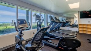 A gym with treadmills and an elliptical machine, large windows with a view, and a flat-screen TV on the wall. - Last minute booking discounts! 2 Bedroom, Beachfront Condo & Free Beach Chairs (Panama City Beach)