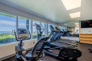 A gym with treadmills and an elliptical machine, large windows with a view, and a flat-screen TV on the wall. - Last minute booking discounts! 2 Bedroom, Beachfront Condo & Free Beach Chairs (Panama City Beach)