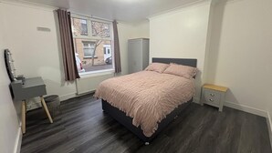 Un dormitorio con cama, escritorio, silla, armario y ventana con cortinas.