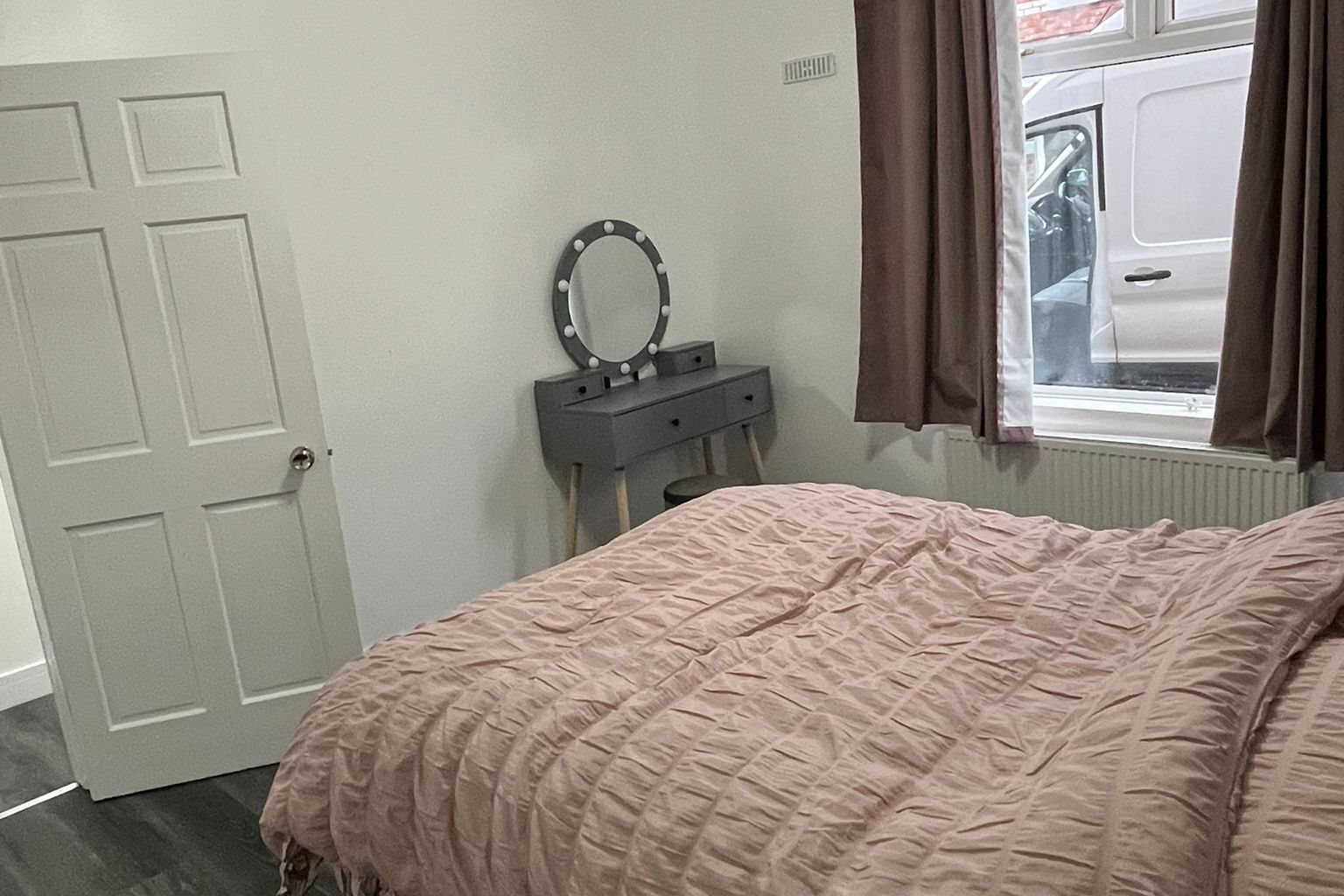 Un dormitorio con cama, cómoda con espejo, puerta y ventana con cortinas.