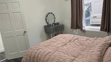 Un dormitorio con cama, cómoda con espejo, puerta y ventana con cortinas.
