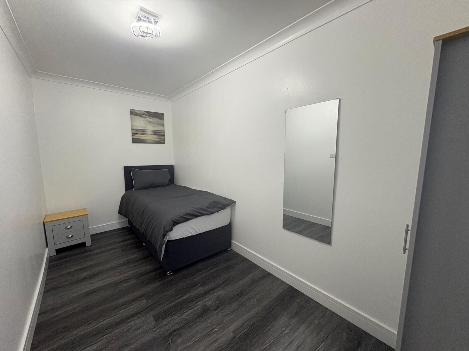 Une chambre à coucher avec un lit, une table de chevet, un miroir et un tableau accroché au mur.