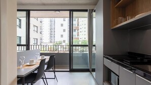A modern kitchen with a black countertop and stainless steel appliances. There is a dining area with a table and chairs, and a large window offering a view of the cityscape. - Comfort and Convenience w/ an Unbeatable Location in Jardim Paulista - Onns (São Paulo)