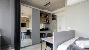 A modern bedroom with a bed, a desk, and a view into a kitchen area. - Comfort and Convenience w/ an Unbeatable Location in Jardim Paulista - Onns (São Paulo)